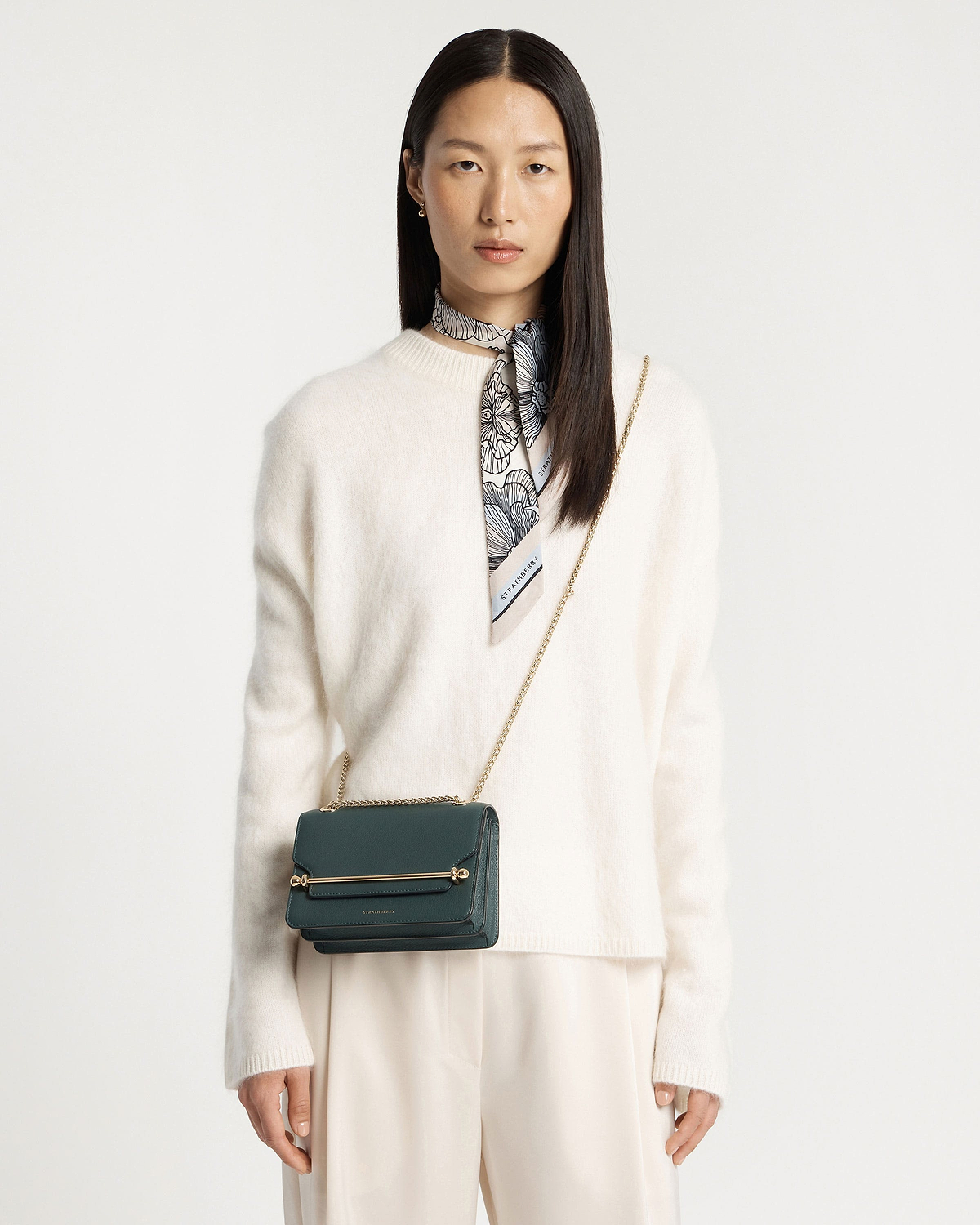 Model wearing cream jumper with bottle green East/West Mini bag and gold chain strap