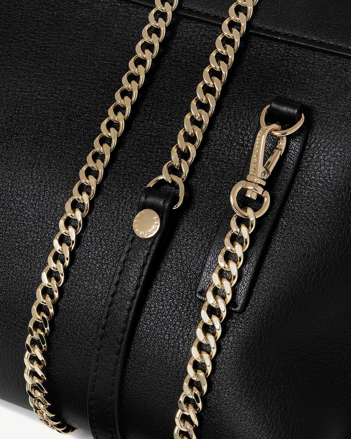 Black leather bag showing two gold chains and a Stella McCartney engraved clasp.