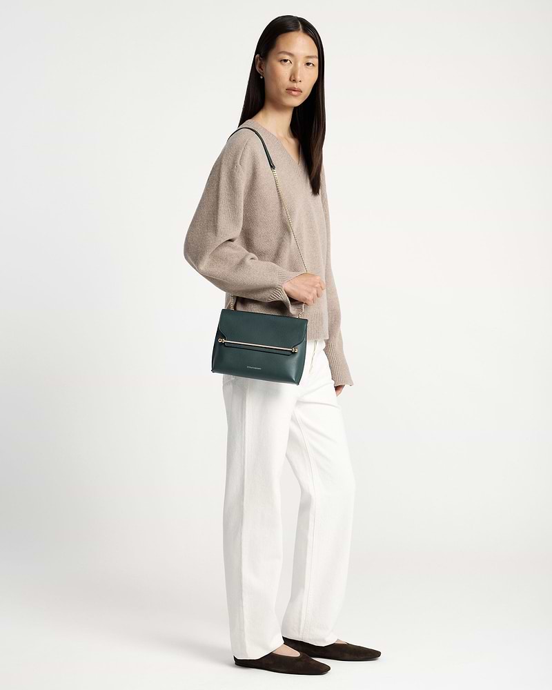 Model wearing bottle green Stylist crossbody bag with gold chain and metal bar.