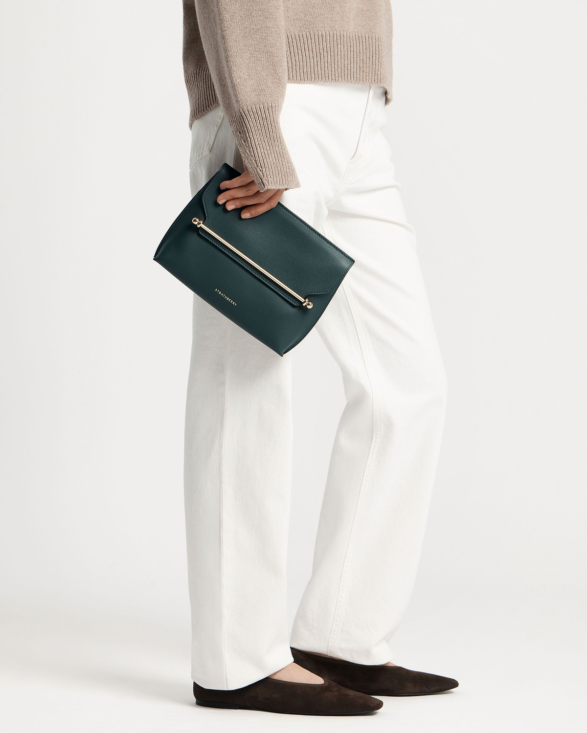 Model holding bottle green Strathberry Stylist clutch with gold bar detail.