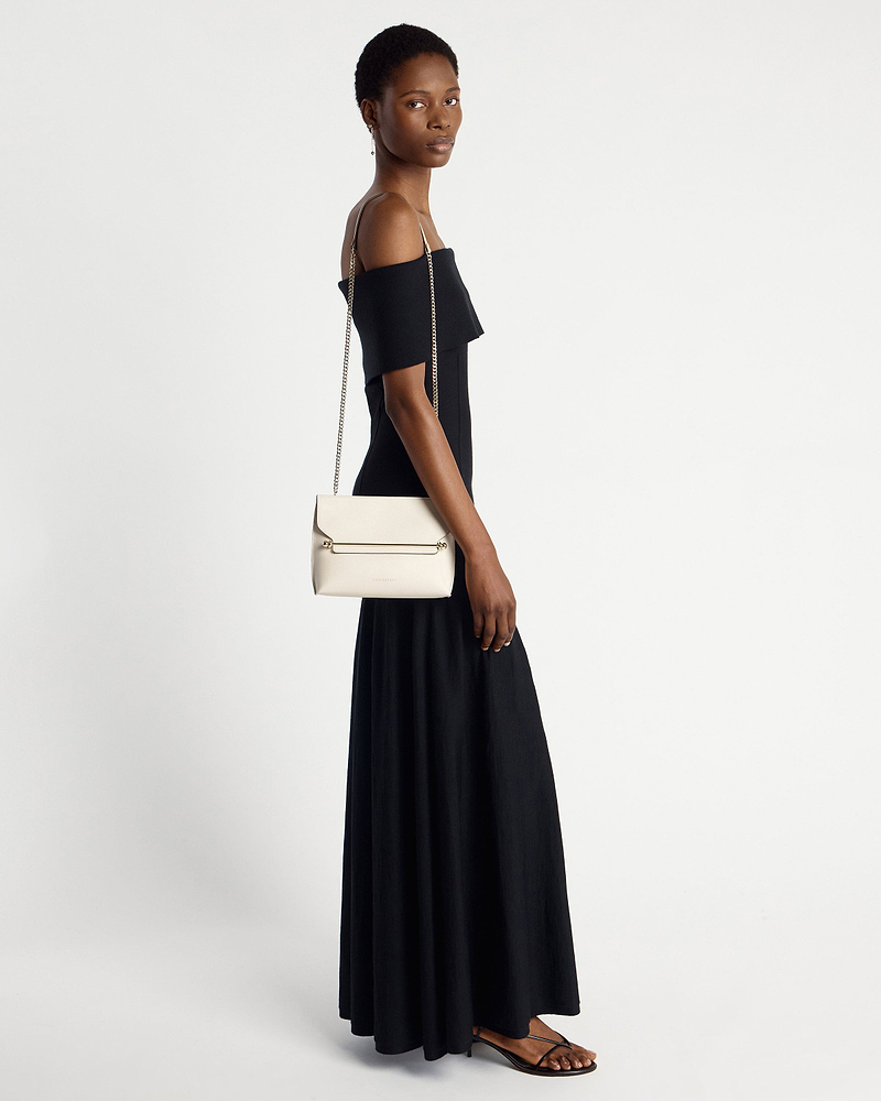 Model wearing black dress carrying vanilla shoulder bag with chain strap.