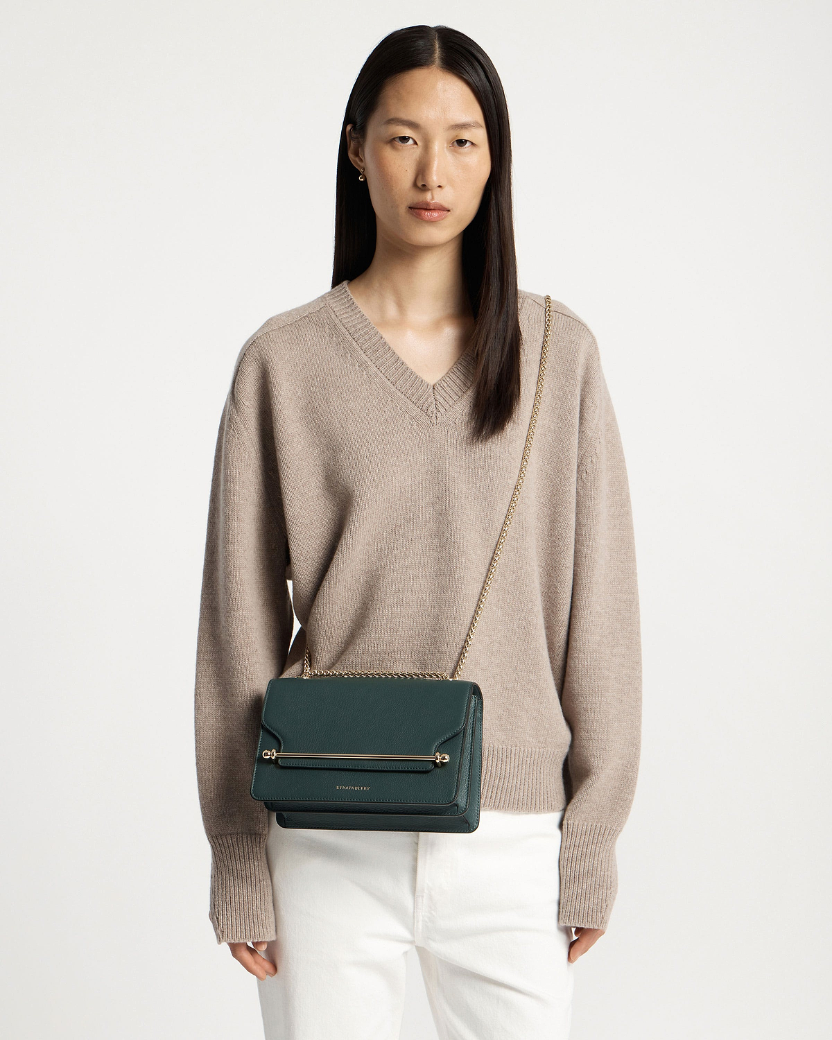 Model wearing bottle-green east/west leather cross-body bag with gold chain strap.