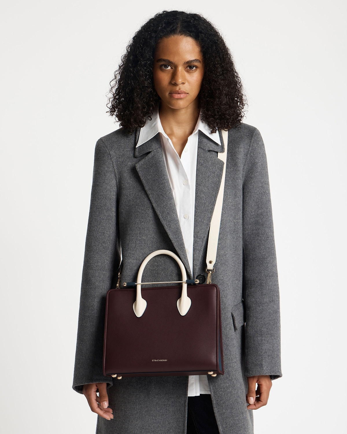 Model carrying a Strathberry midi tote in burgundy, navy and vanilla.