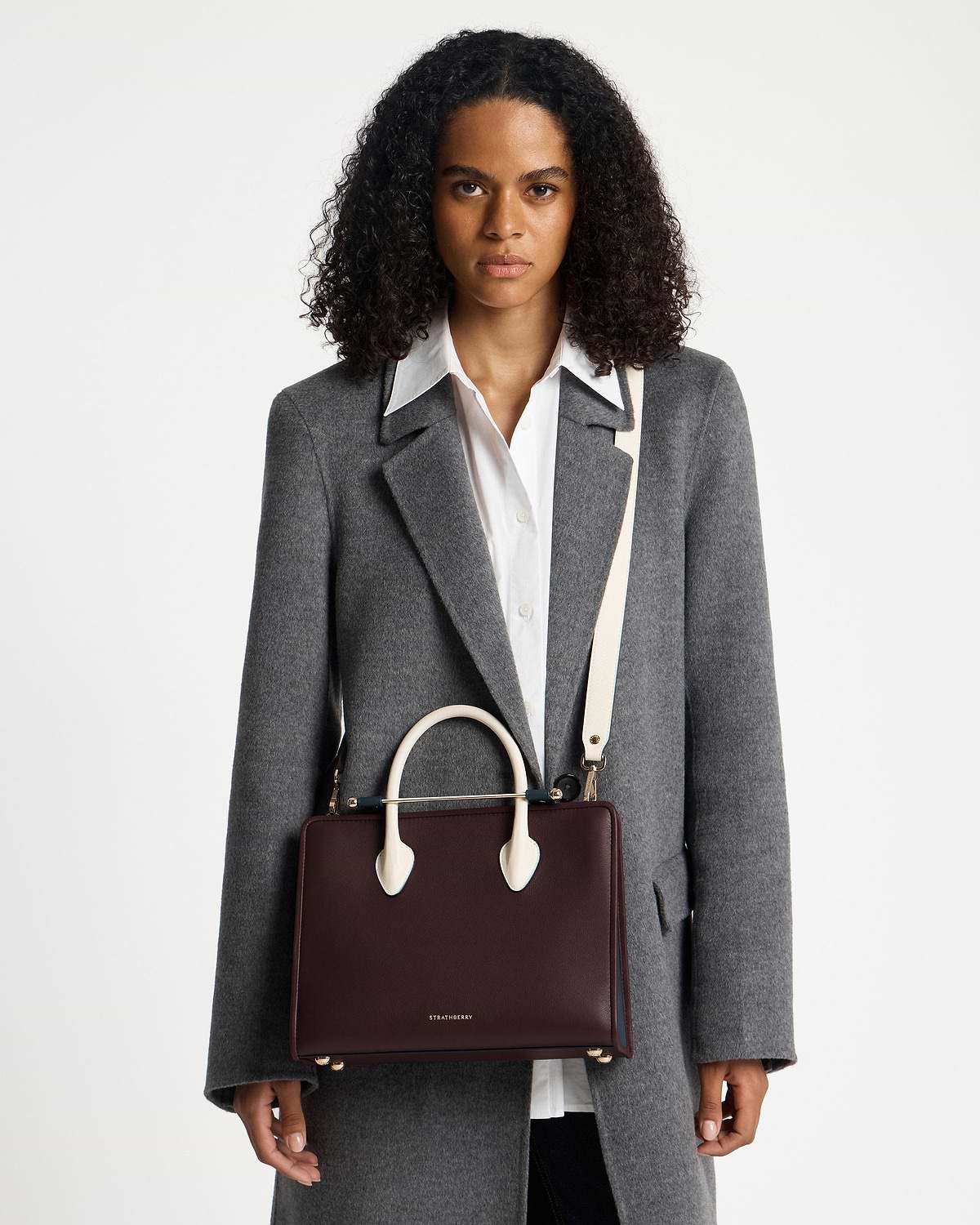 Model carrying a Strathberry midi tote in burgundy, navy and vanilla.