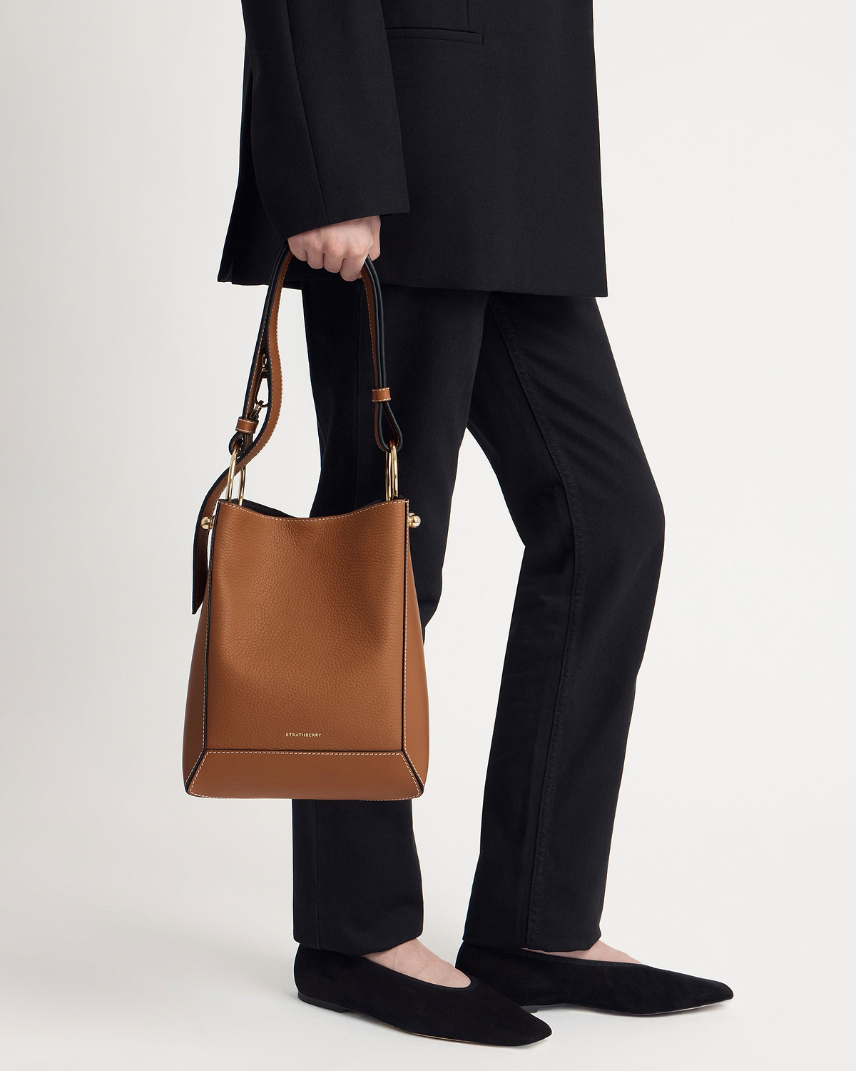Model's lower body holding a Strathberry tan leather midi bucket bag with vanilla stitching.
