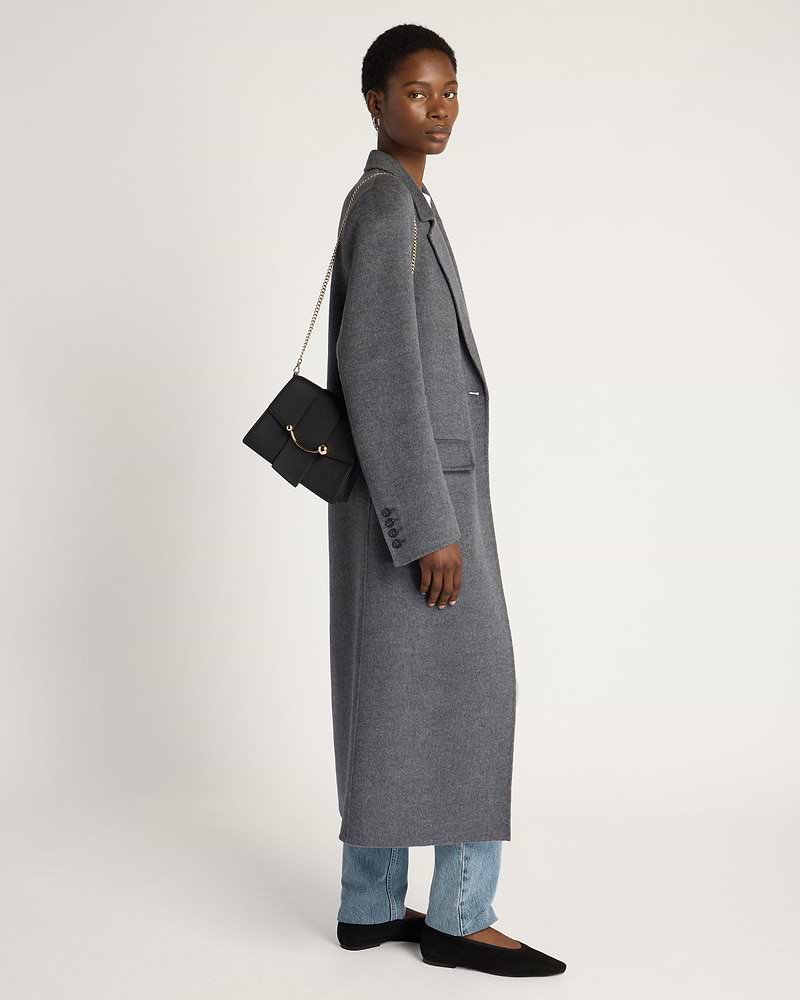 Model in grey long coat carrying black Box Crescent bag with gold chain