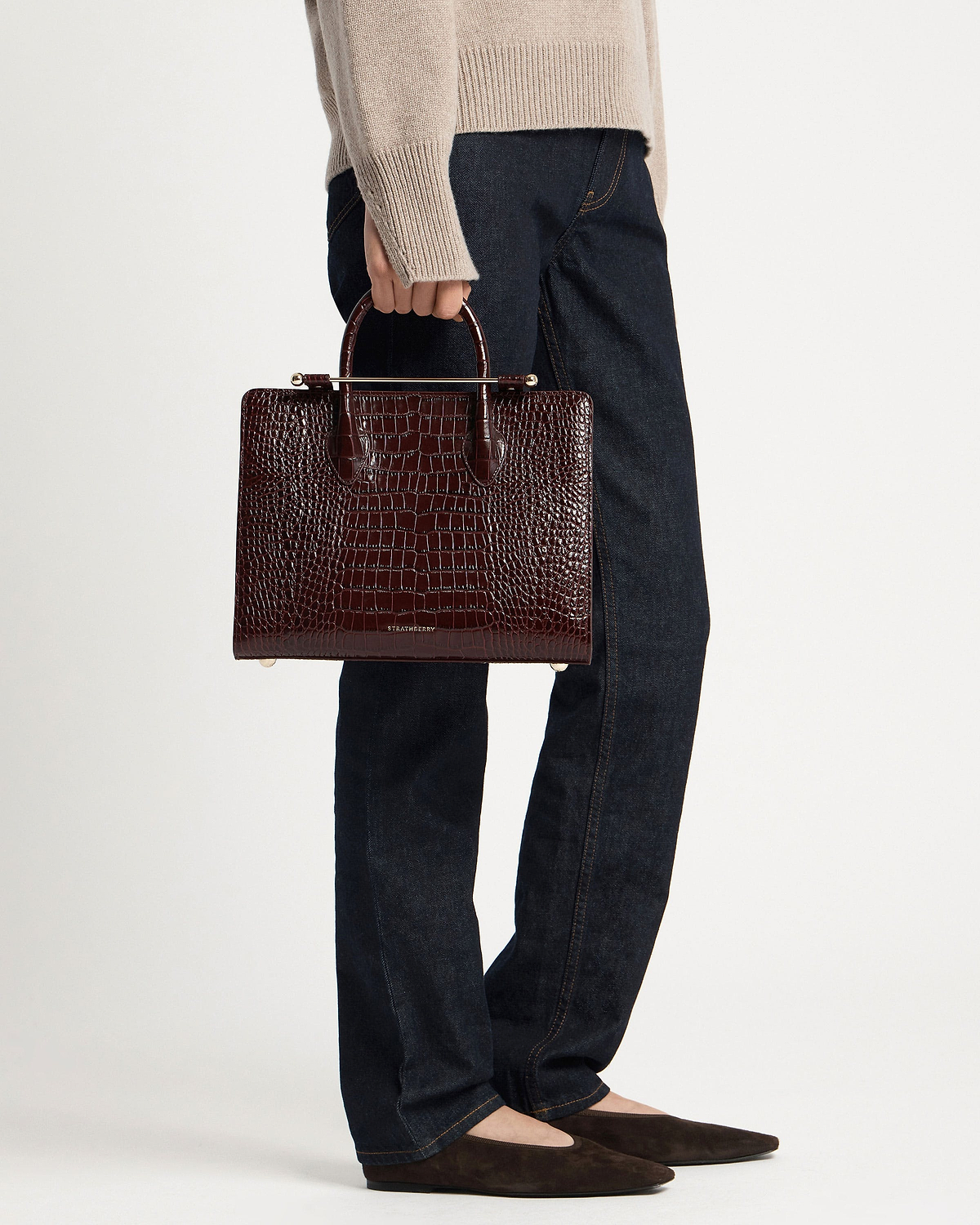 Model holding Strathberry croc-embossed midi tote in dark brown with gold hardware