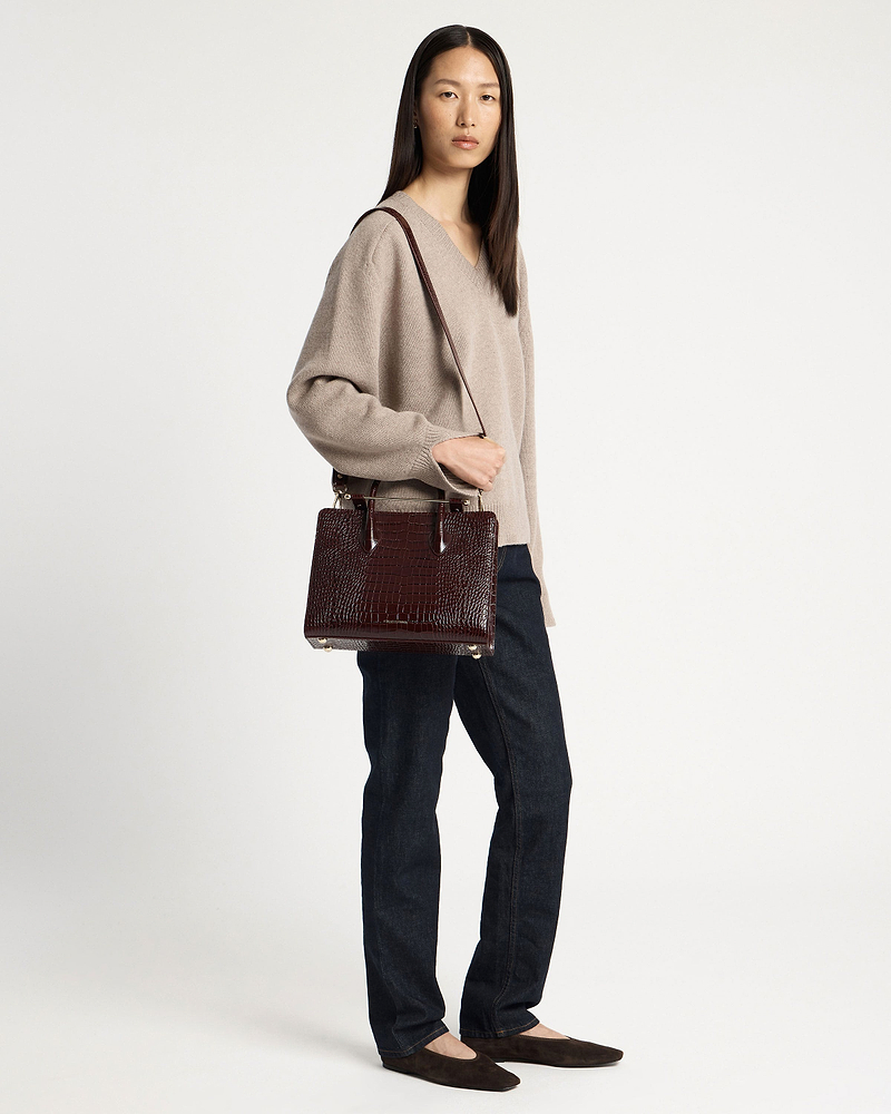 Woman wearing a beige sweater and jeans holding a croc-embossed midi tote bag.
