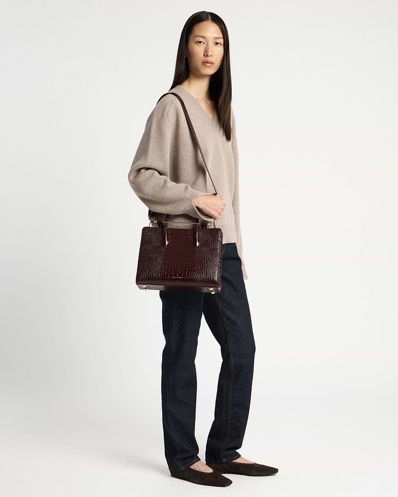 Woman wearing a beige sweater and jeans holding a croc-embossed midi tote bag.