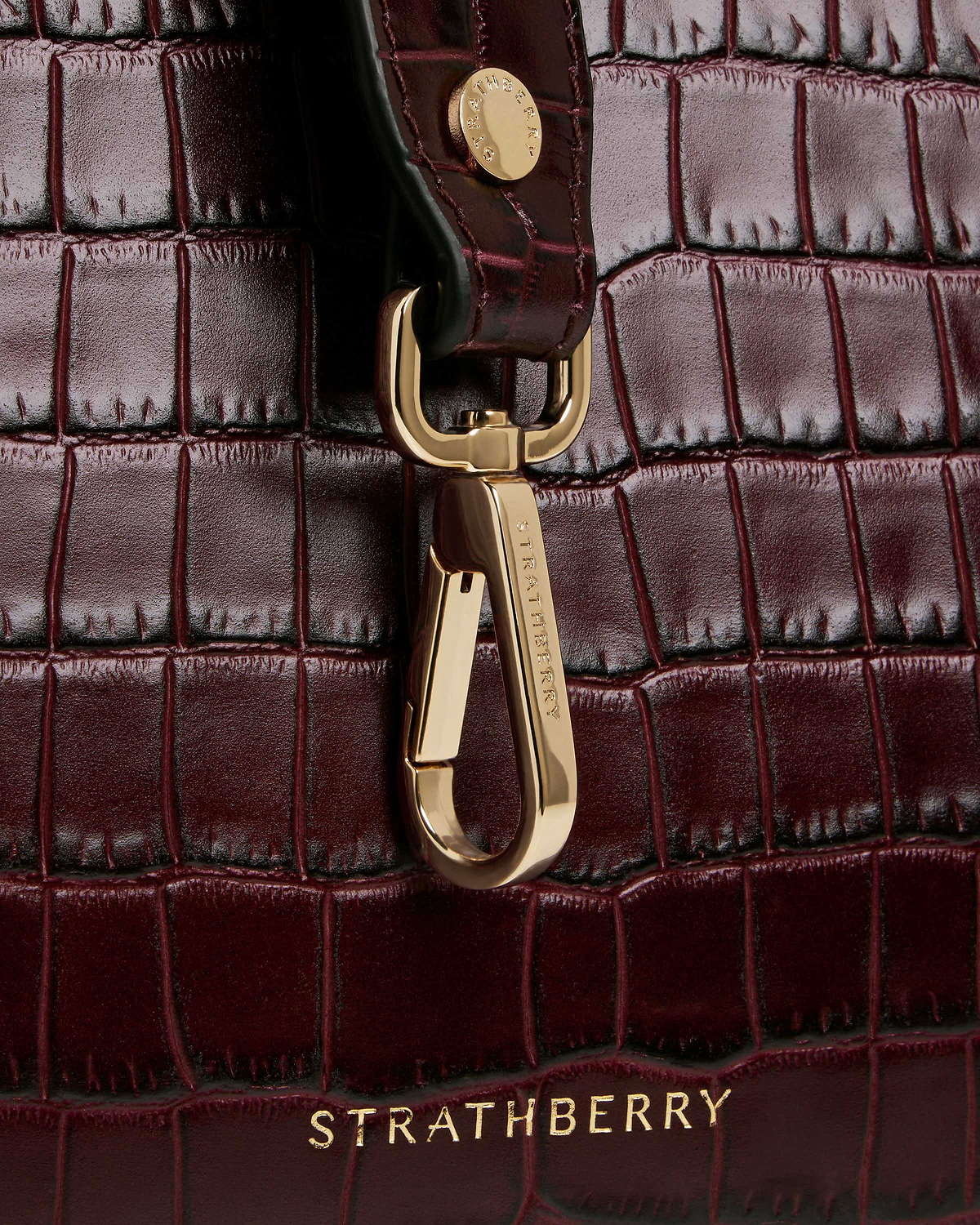 Burgundy croc midi tote close-up showing gold clasp and Strathberry logo.