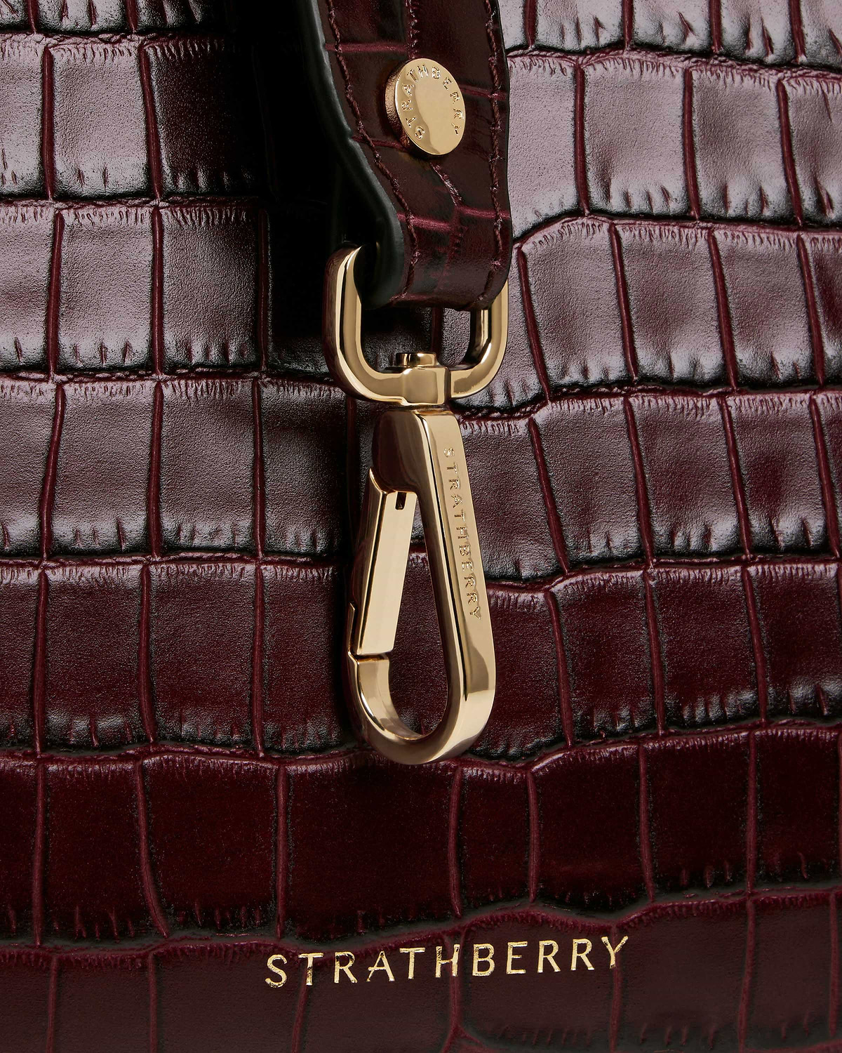 Burgundy croc midi tote close-up showing gold clasp and Strathberry logo.