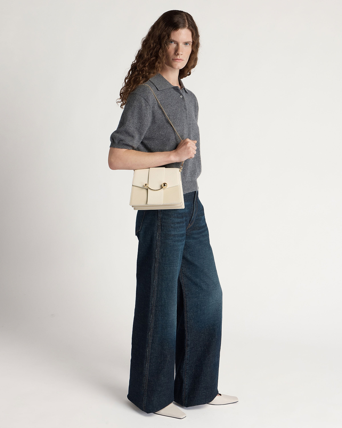 Model wearing grey short-sleeve top and wide-leg jeans, holding a vanilla box crescent bag.