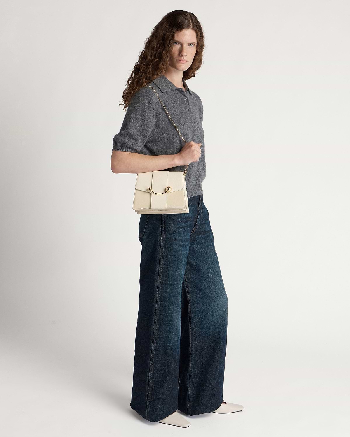 Model wearing grey short-sleeve top and wide-leg jeans, holding a vanilla box crescent bag.