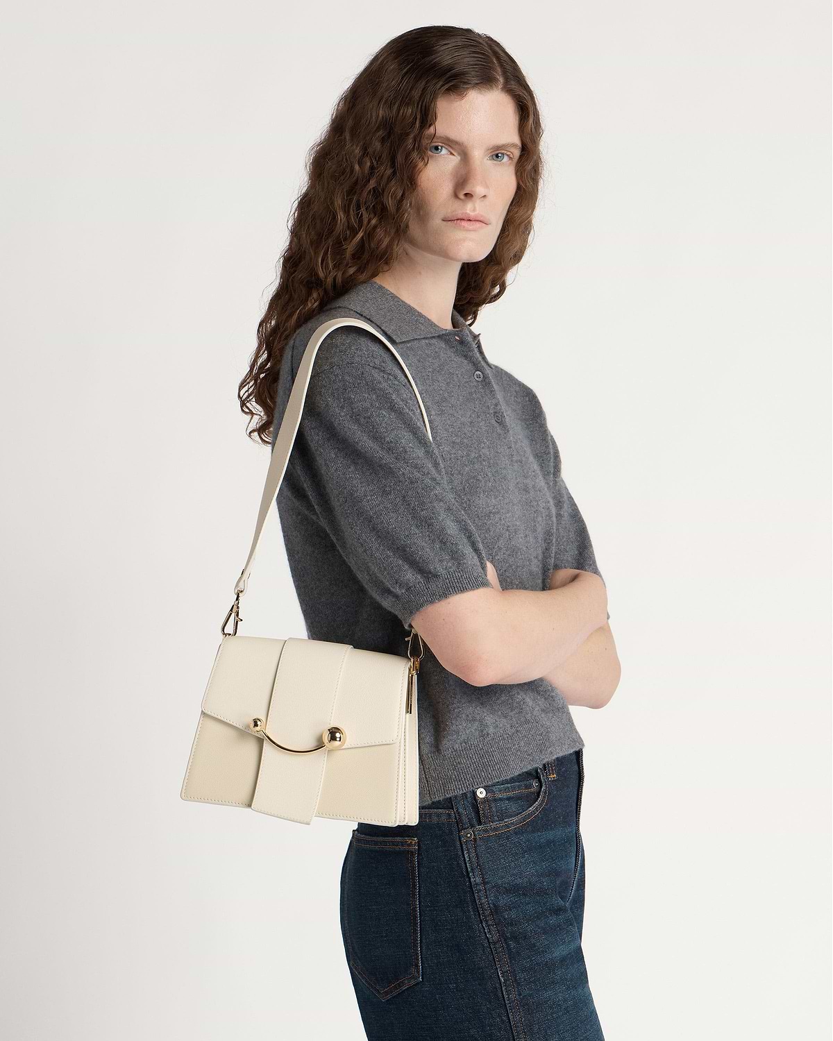 Woman in grey sweater carries vanilla Box Crescent shoulder bag with gold clasp.