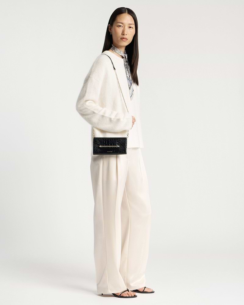 Model wearing a black crocodile-effect chain wallet with a gold chain strap.