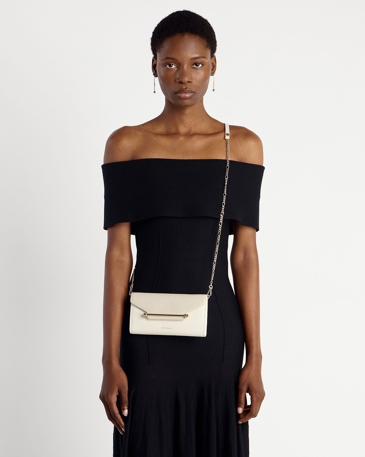 Model wearing black off-shoulder dress with Strathberry Multrees chain wallet in vanilla diamond.