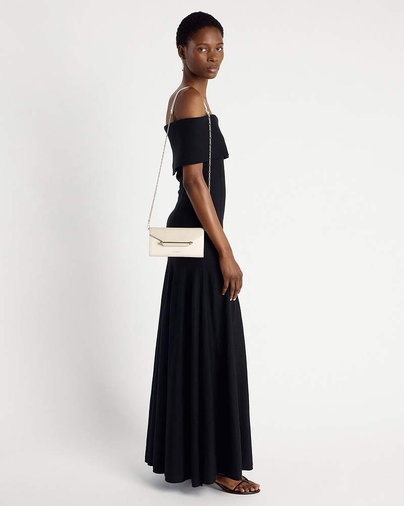 Model wearing black off-shoulder dress carries vanilla diamond chain wallet on shoulder.