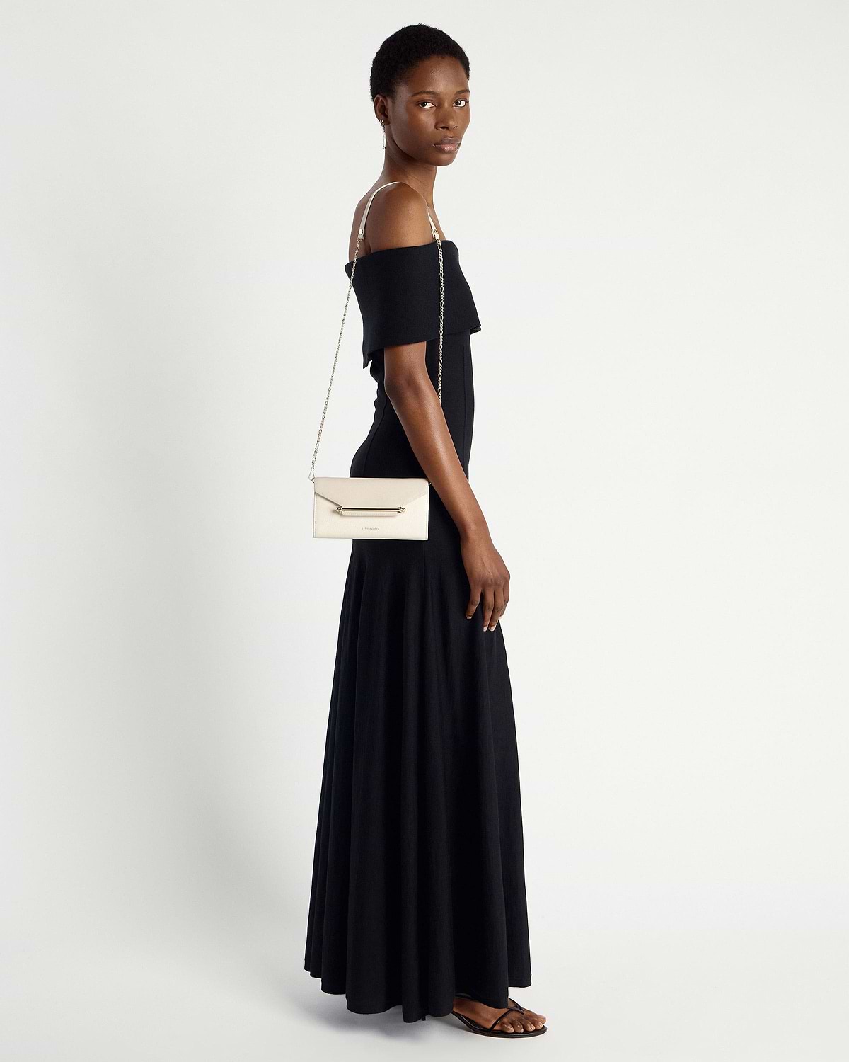 Model wearing black off-shoulder dress carries vanilla diamond chain wallet on shoulder.