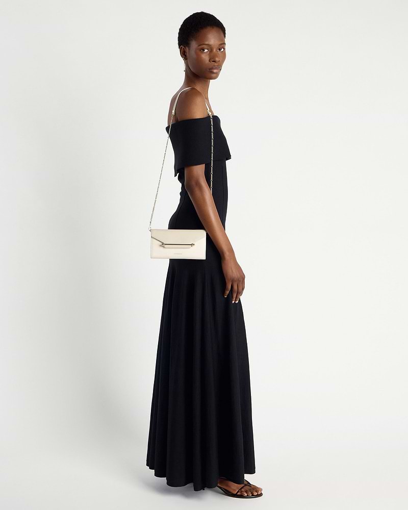 Model wearing black off-shoulder dress carries vanilla diamond chain wallet on shoulder.