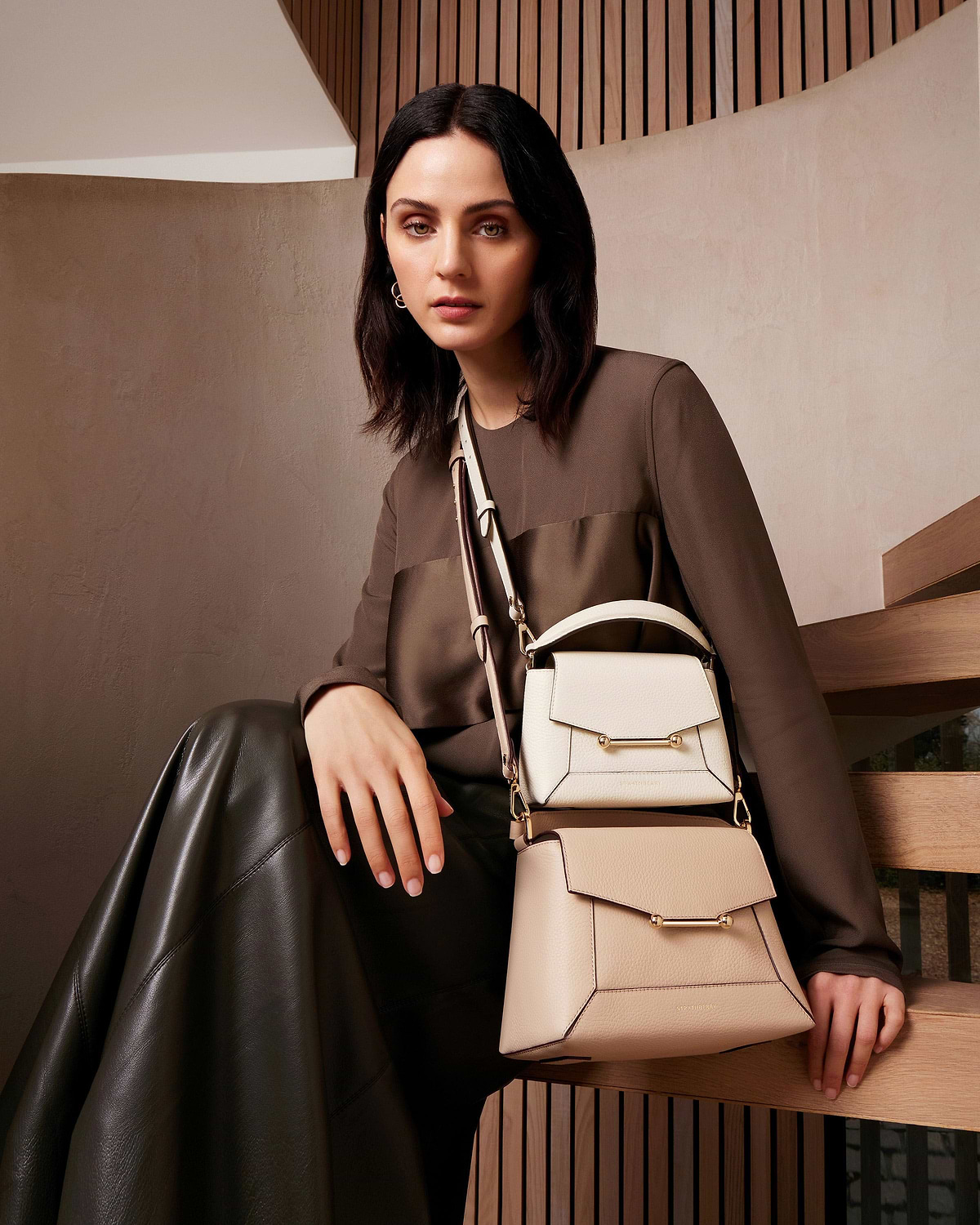Model seated wearing brown top holds two mosaic bags in oat and cream.