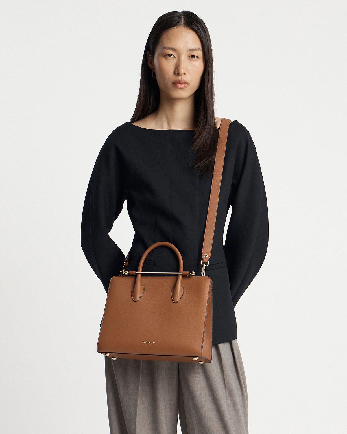 Model wearing Strathberry chestnut midi tote with top handles and shoulder strap.