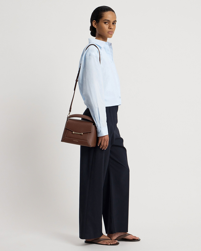 Model wearing a light blue shirt carrying a chocolate mosaic bag with vanilla stitch.