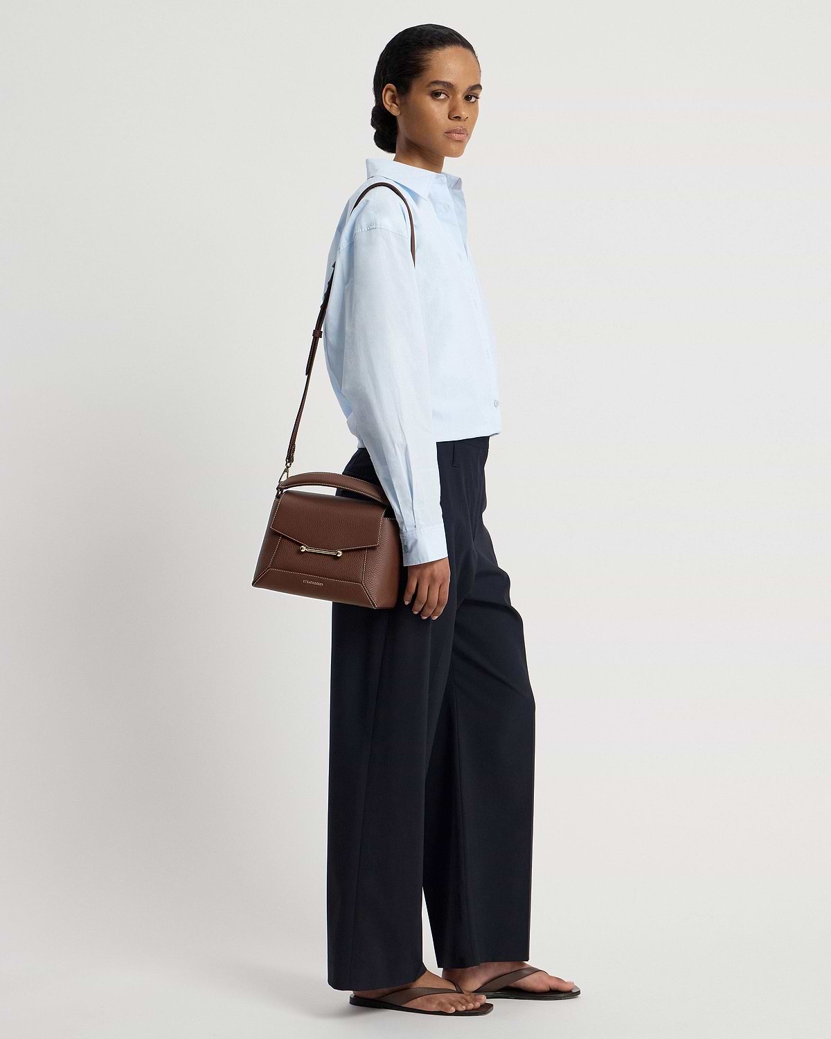 Model wearing a light blue shirt carrying a chocolate mosaic bag with vanilla stitch.