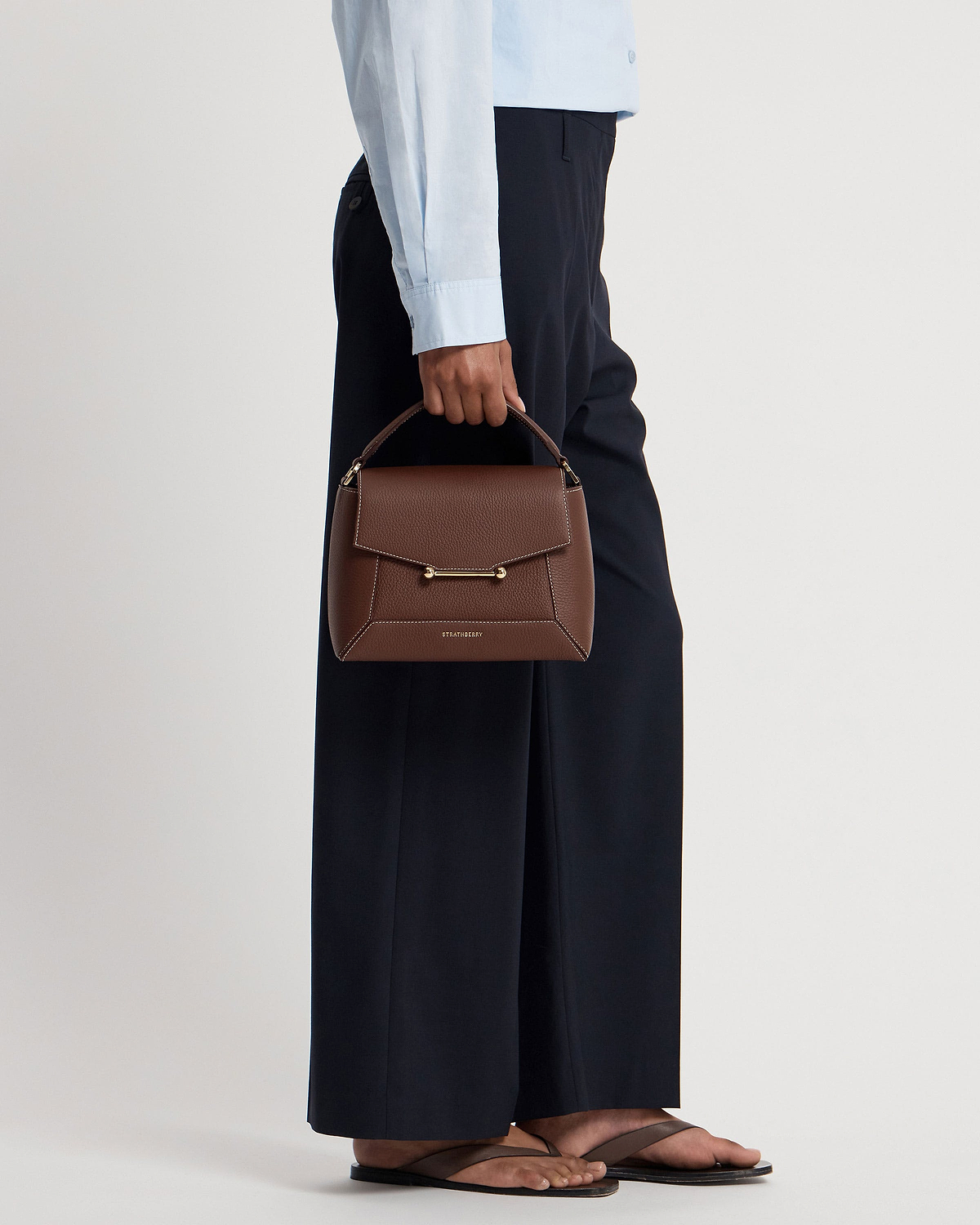 Model's lower body holding chocolate Mosaic Bag with vanilla stitching and Strathberry logo.
