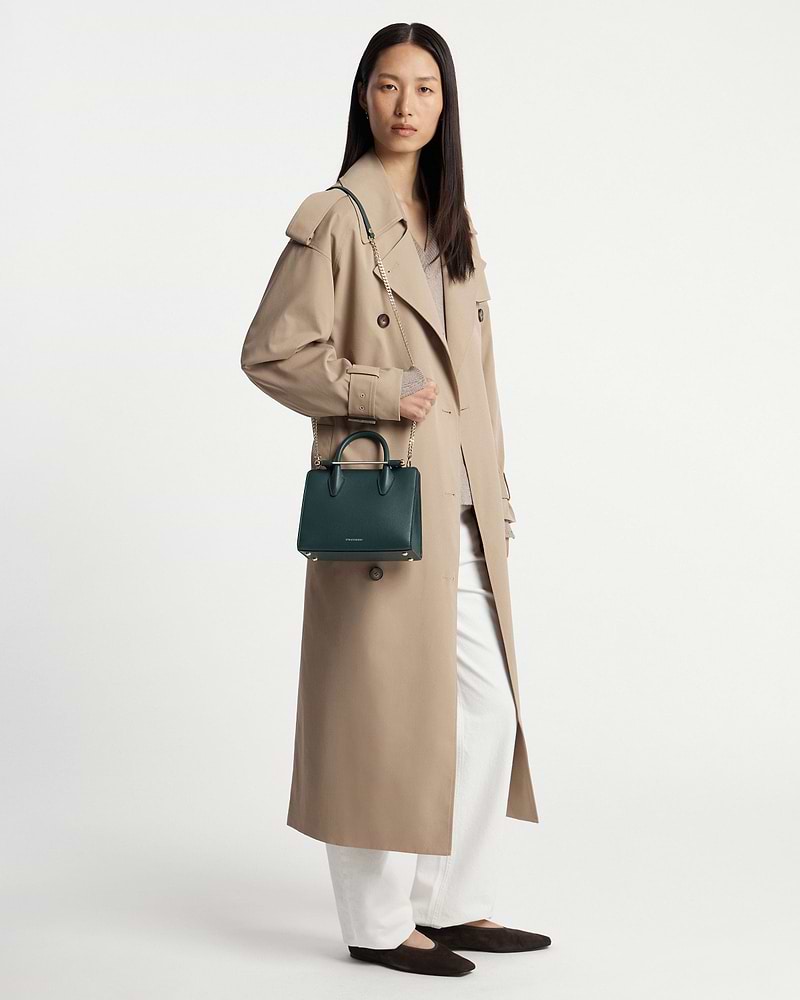Woman in beige trench coat holding bottle green mini tote with chain shoulder strap.