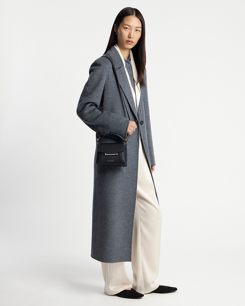 Model in long grey coat and cream trousers holding black Mosaic Nano crossbody bag.
