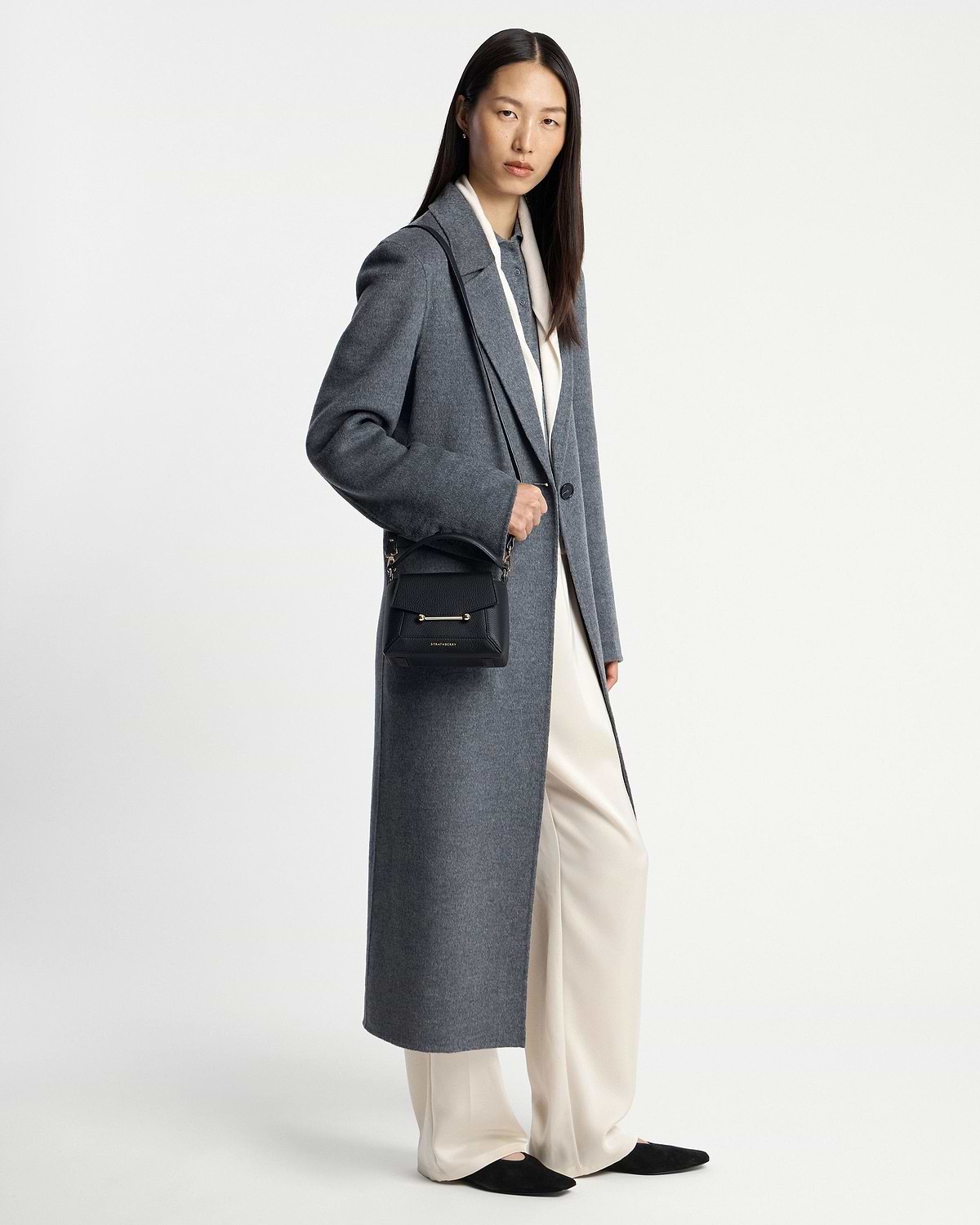 Model in long grey coat and cream trousers holding black Mosaic Nano crossbody bag.