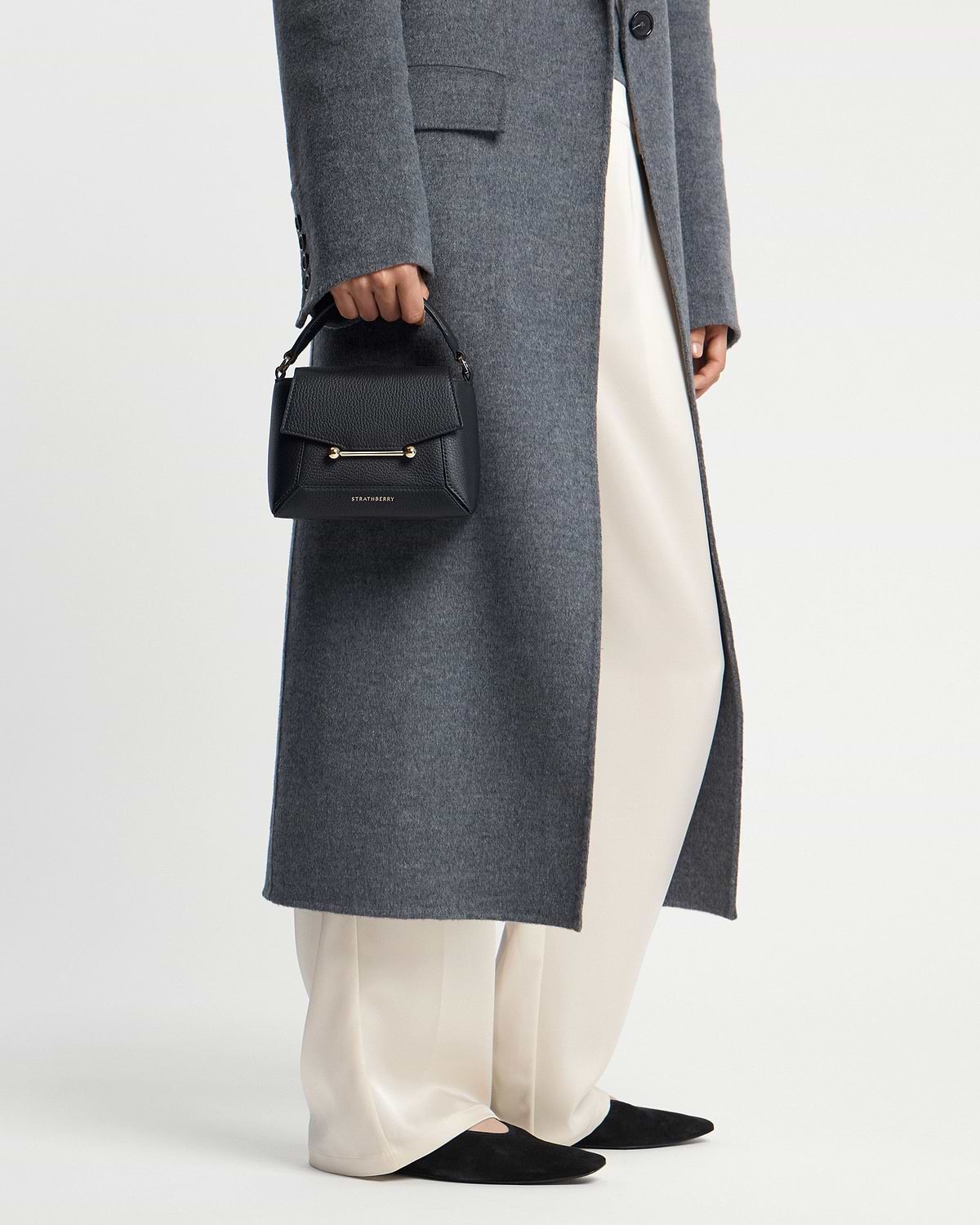 Model holding black Strathberry mini top-handle bag with gold bar detail.
