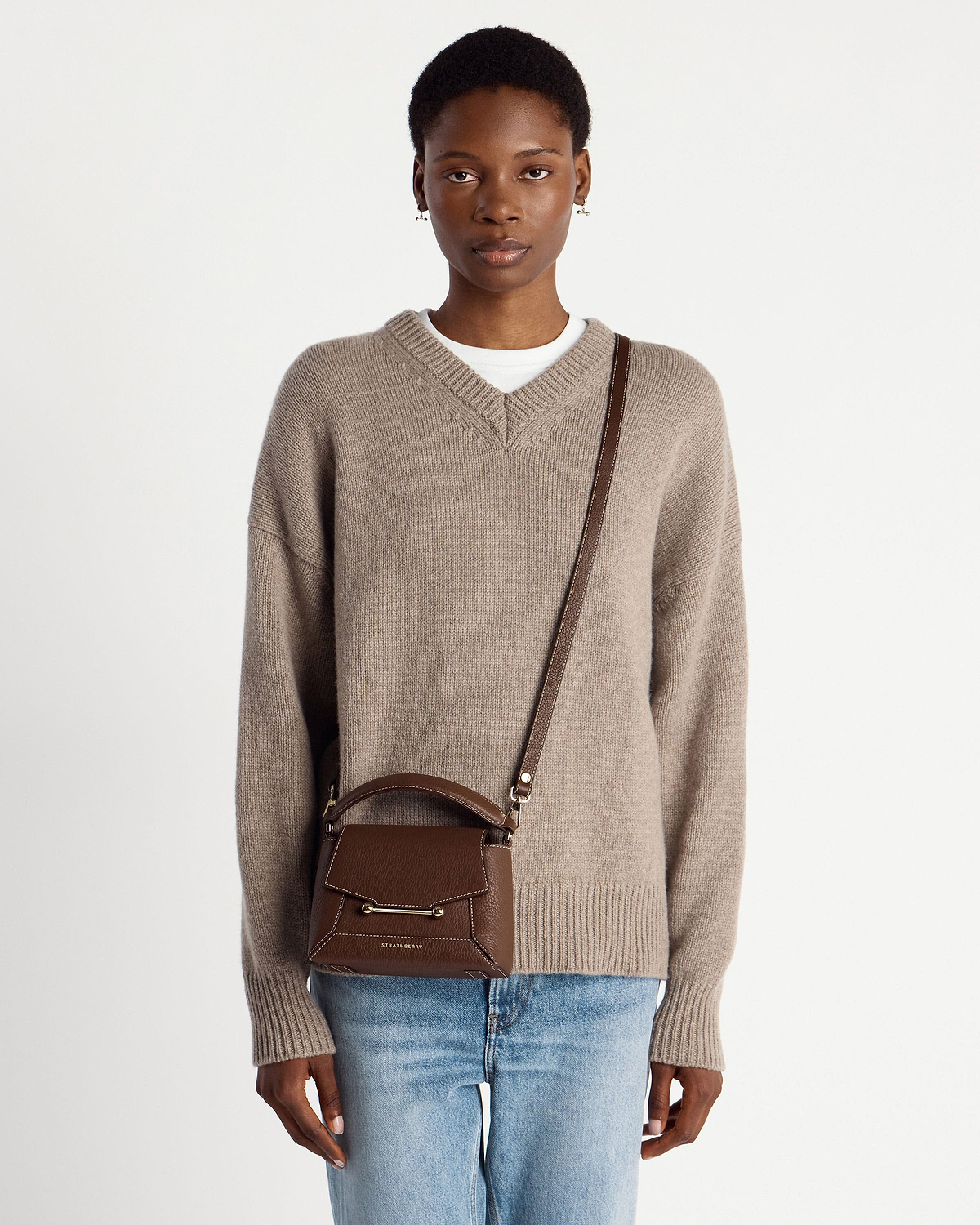 Model wearing chocolate brown leather mini bag with vanilla contrast stitching, top handle and strap.