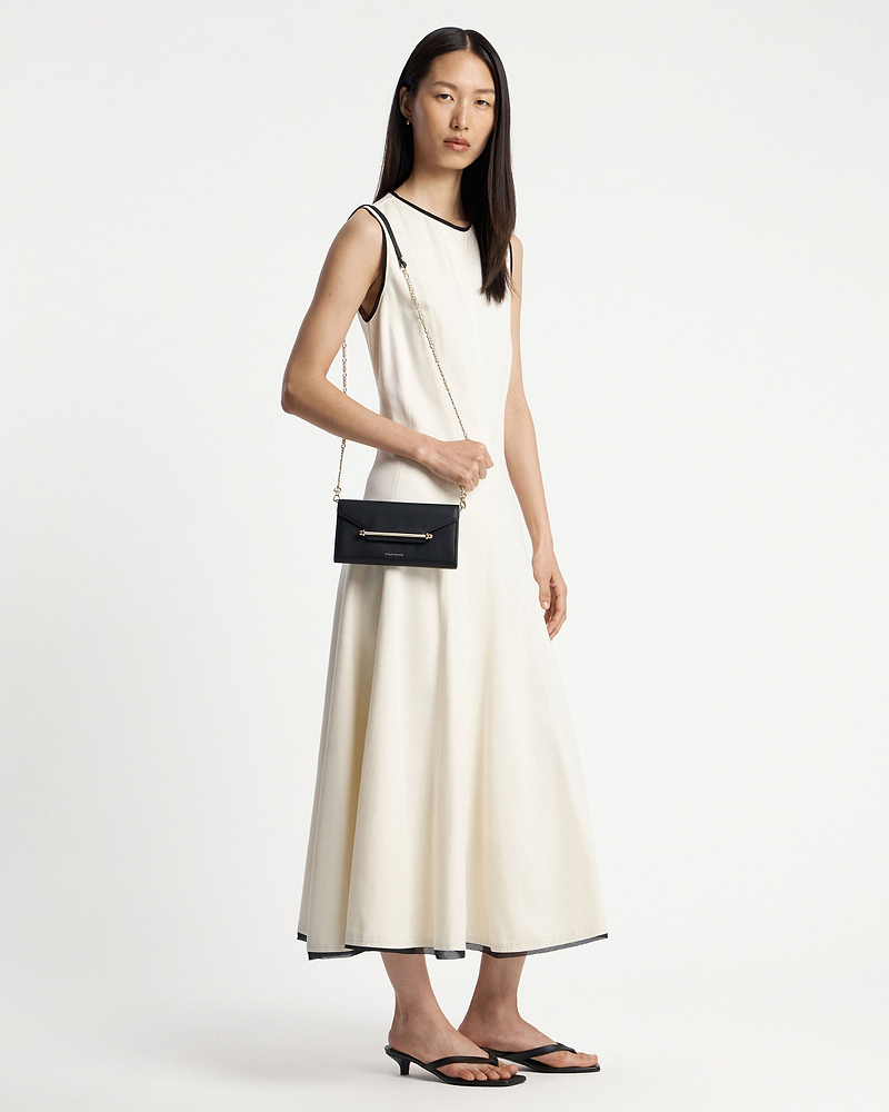 Model in cream sleeveless dress wearing a black chain wallet on a gold shoulder chain.