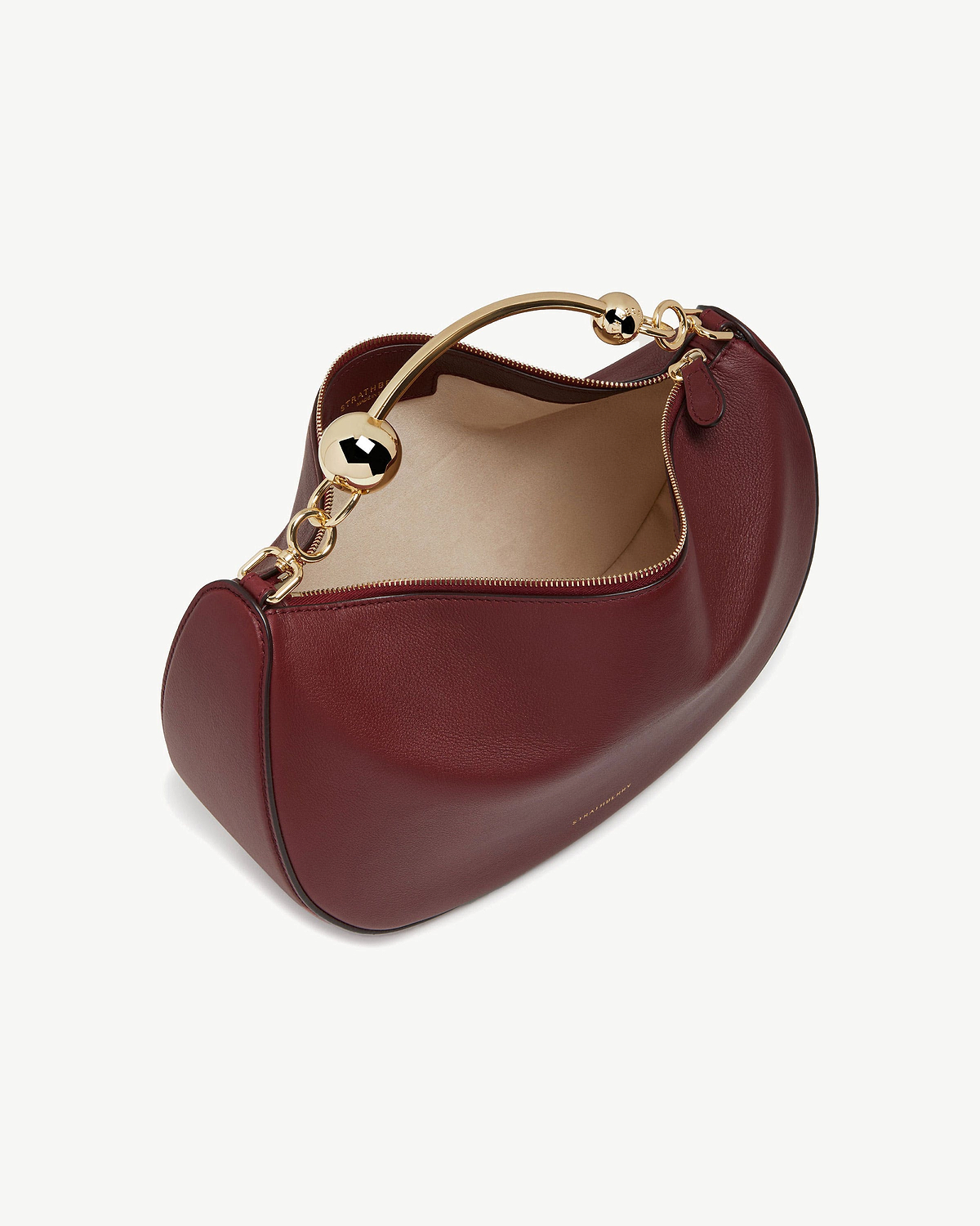 Oxblood leather crescent bag with gold curved top handle and beige interior.
