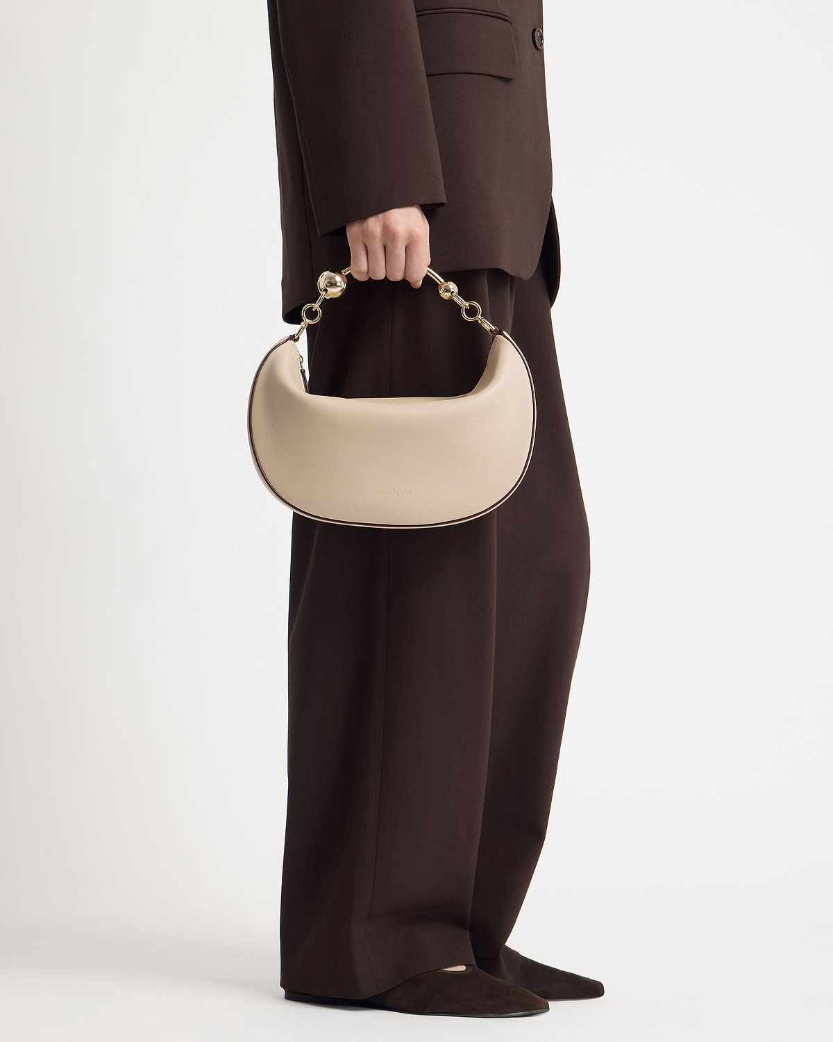 Model holding oat-coloured crescent bag with short gold link handle at side