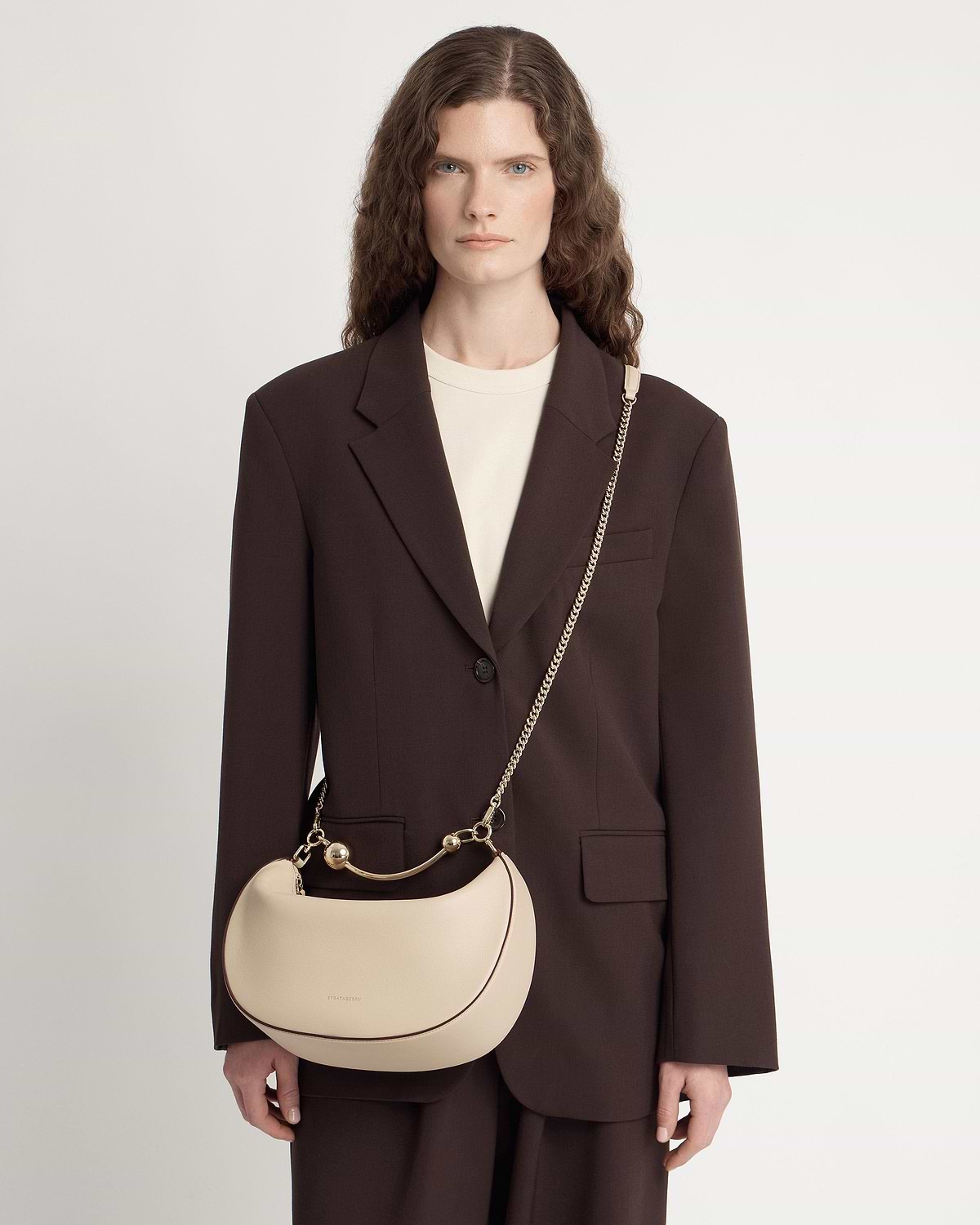 Model wearing oat crescent moon bag with gold chain strap and handle.