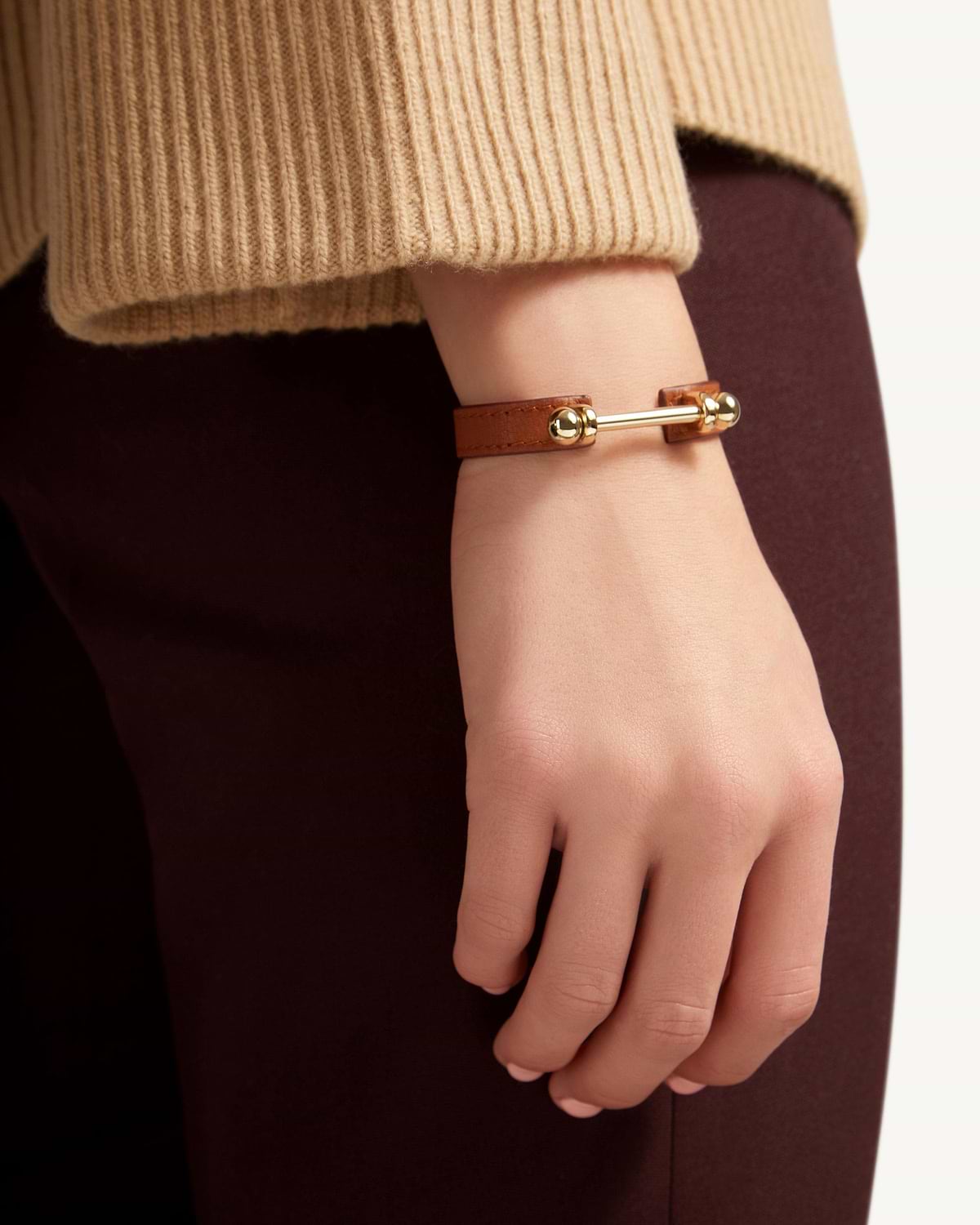 Chestnut leather music bar bracelet with 22-carat gold bar on model's wrist.