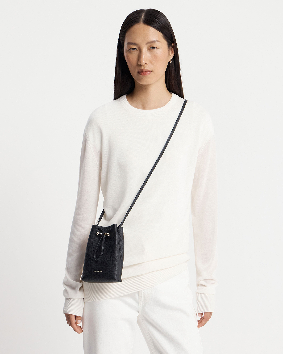 Model wearing a black Strathberry Osette midi pouch crossbody over white jumper.