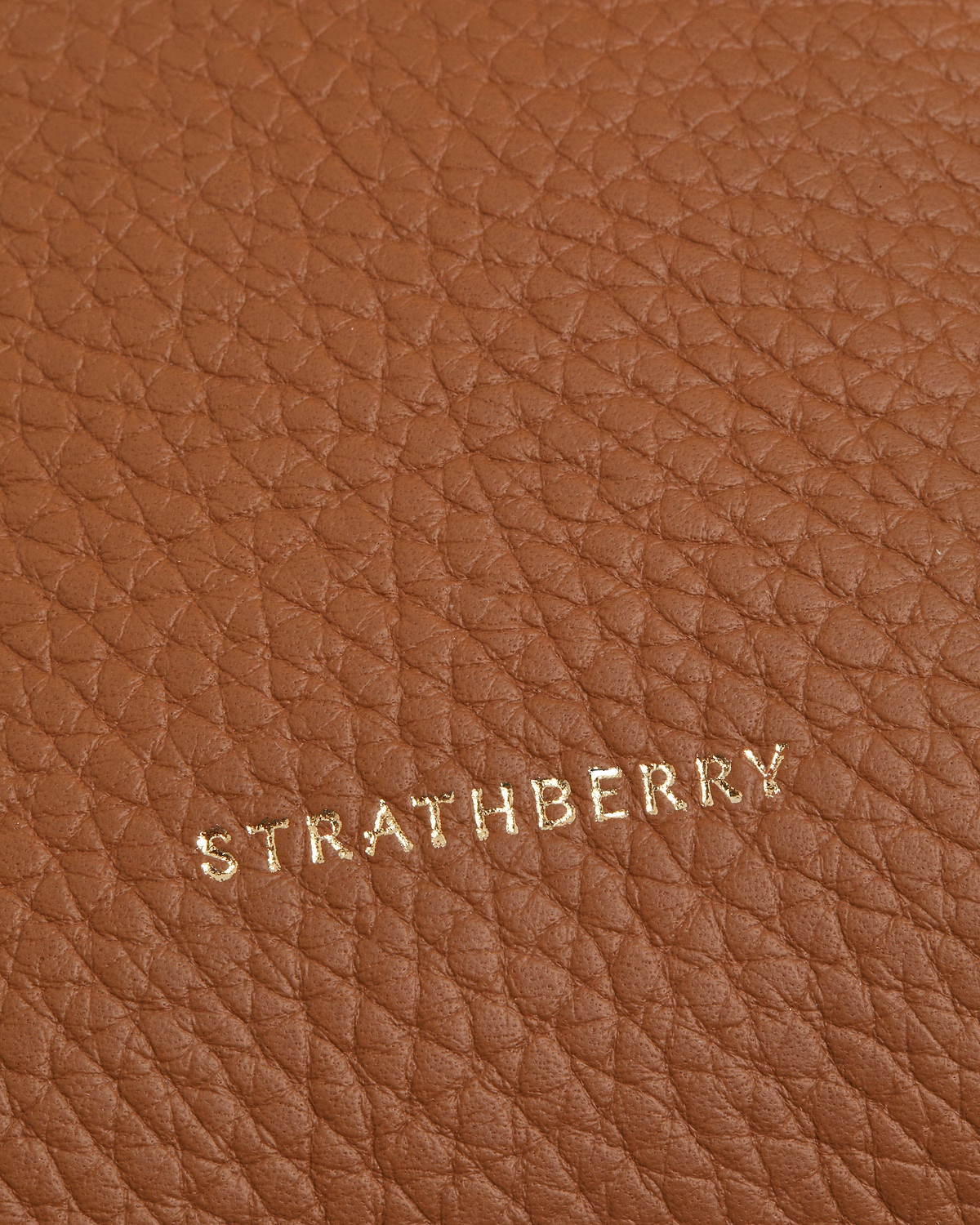 Close-up of tan pebbled leather with gold Strathberry logo lettering.