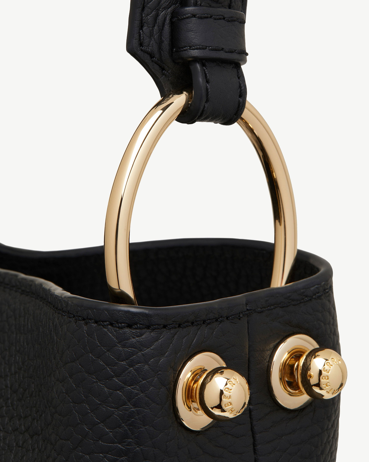 Black leather bag trim with gold ring and visible Burberry studs.
