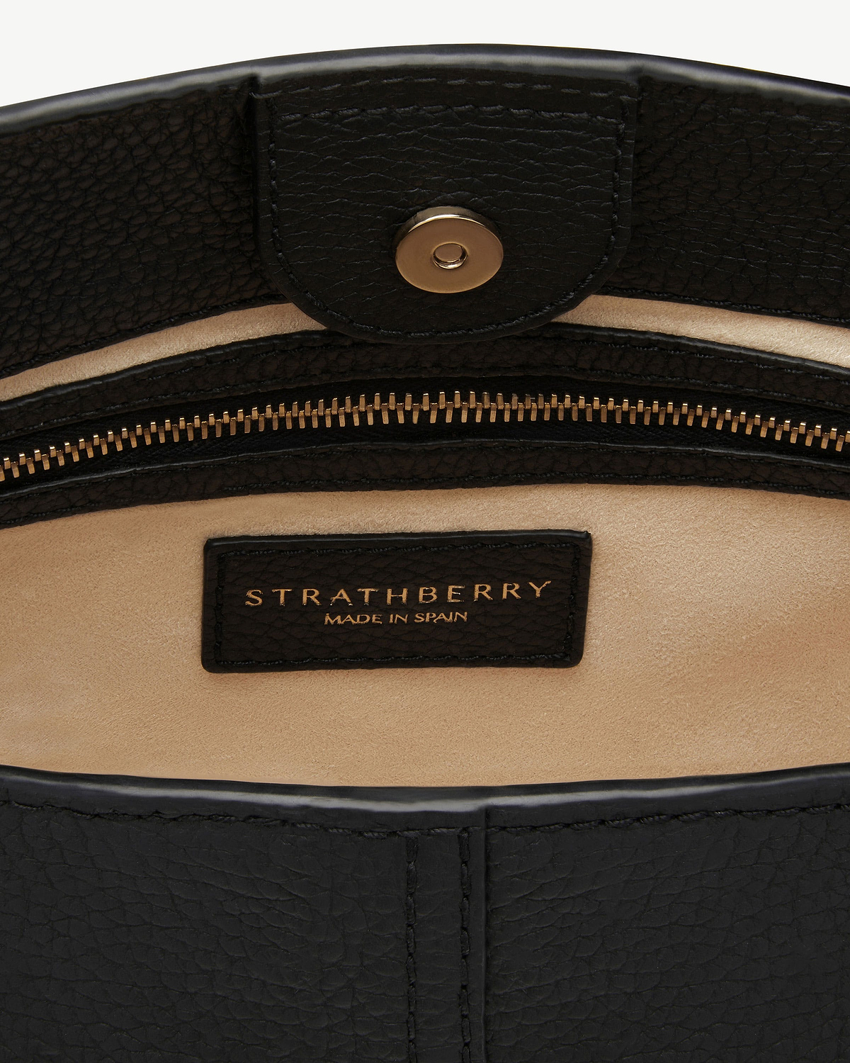 Interior of black leather bag showing Strathberry label, zip and magnetic snap.