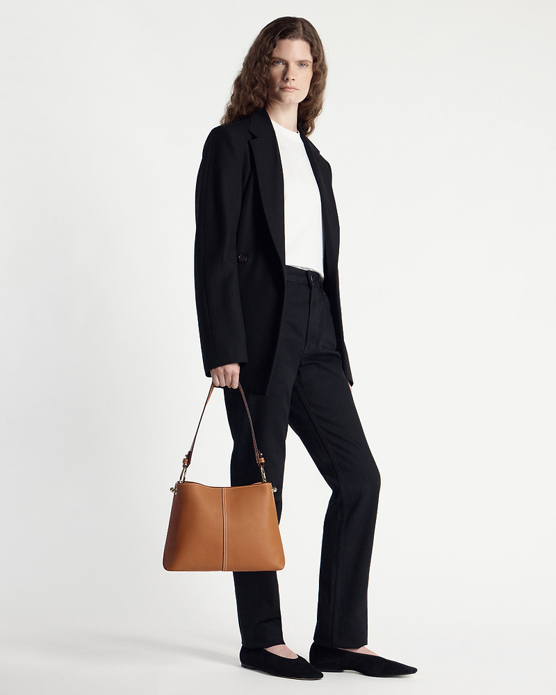 Model in a black blazer and trousers holding a tan hobo bag at her side.