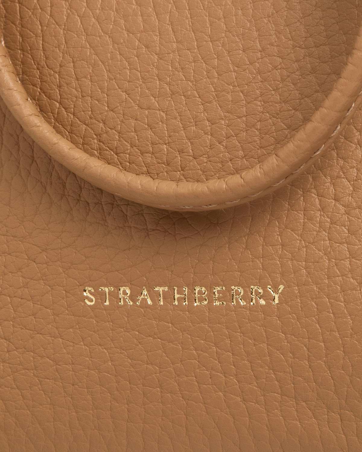 Strathberry logo stamped on caramel pebbled leather midi pouch near handle edge.