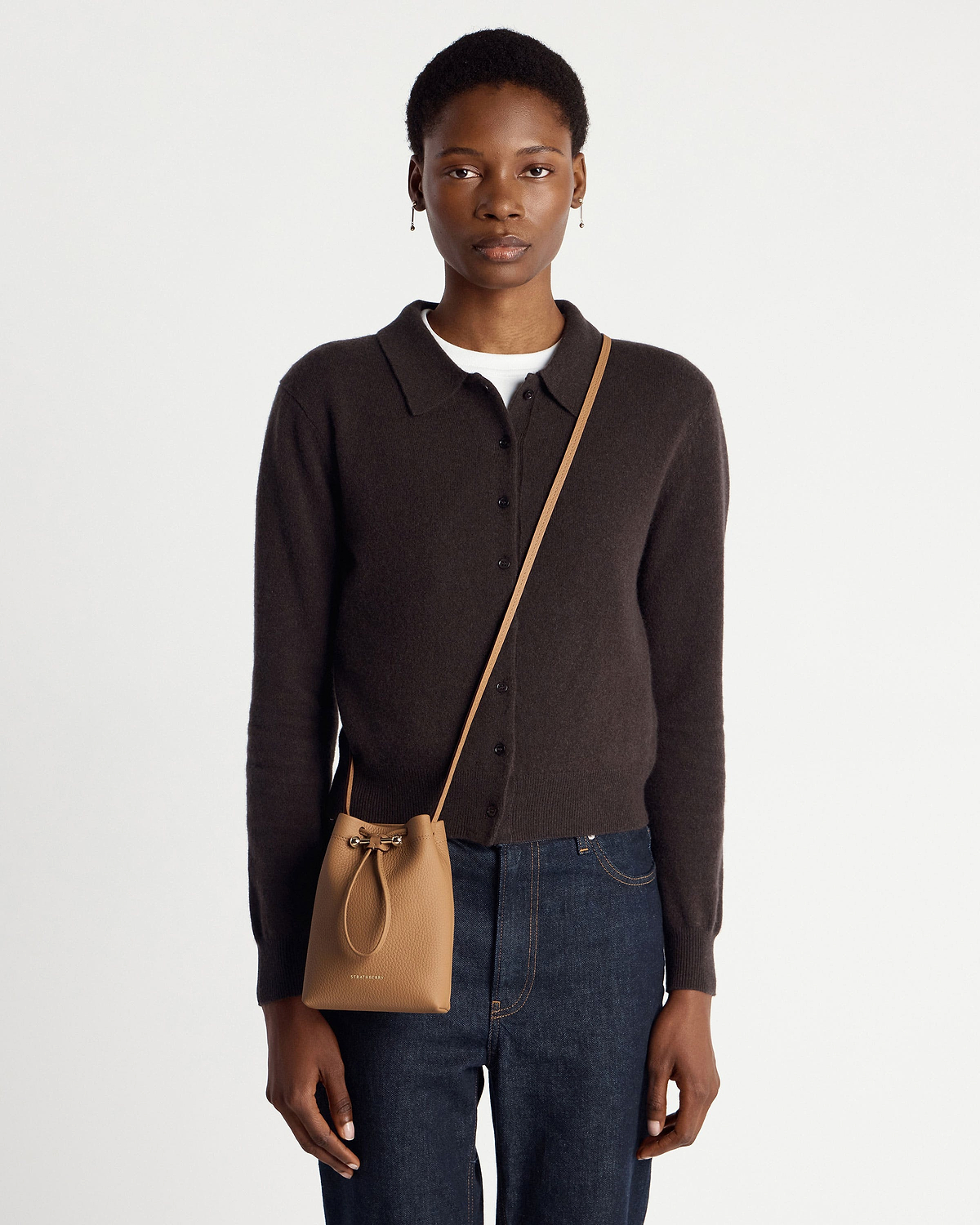Model wearing a caramel leather drawstring crossbody pouch hanging at hip.