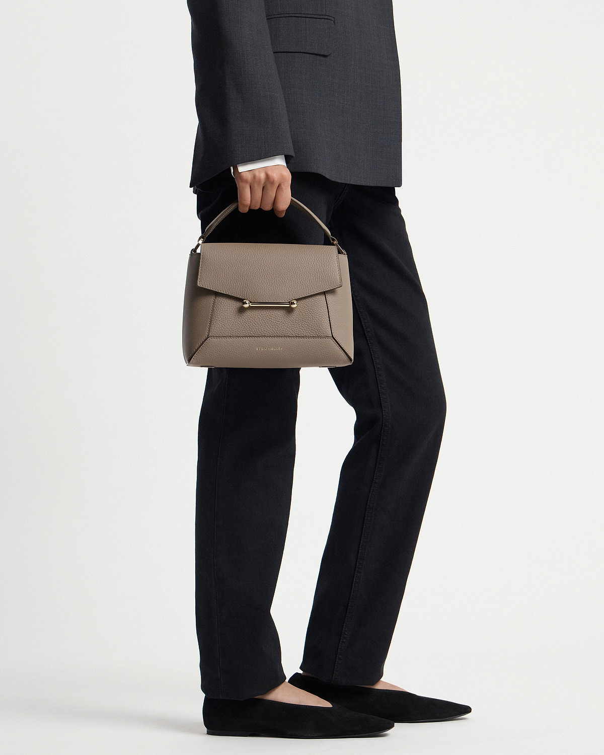 Model holding taupe mosaic bag by top handle, grey blazer and black trousers visible.