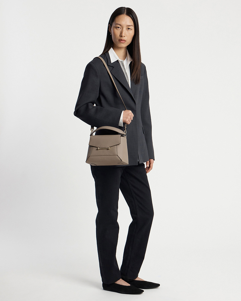 Model wearing dark blazer and black trousers holding taupe mosaic bag