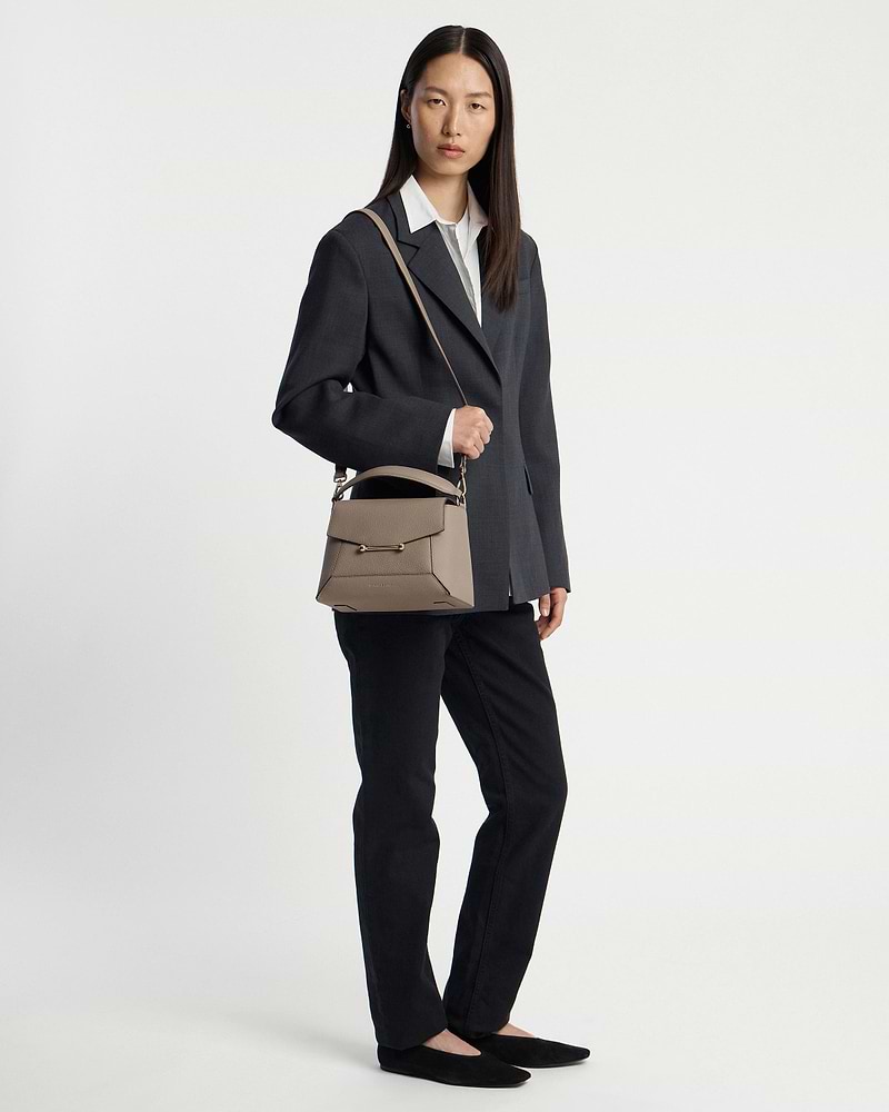 Model wearing dark blazer and black trousers holding taupe mosaic bag