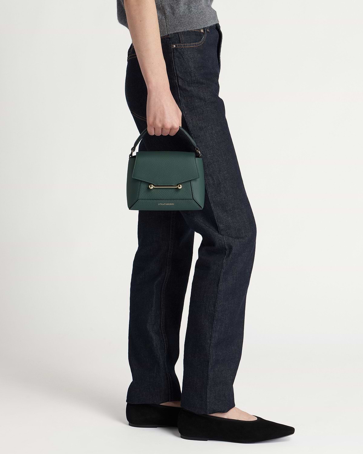 Model holding bottle green Strathberry leather top-handle handbag by her side.