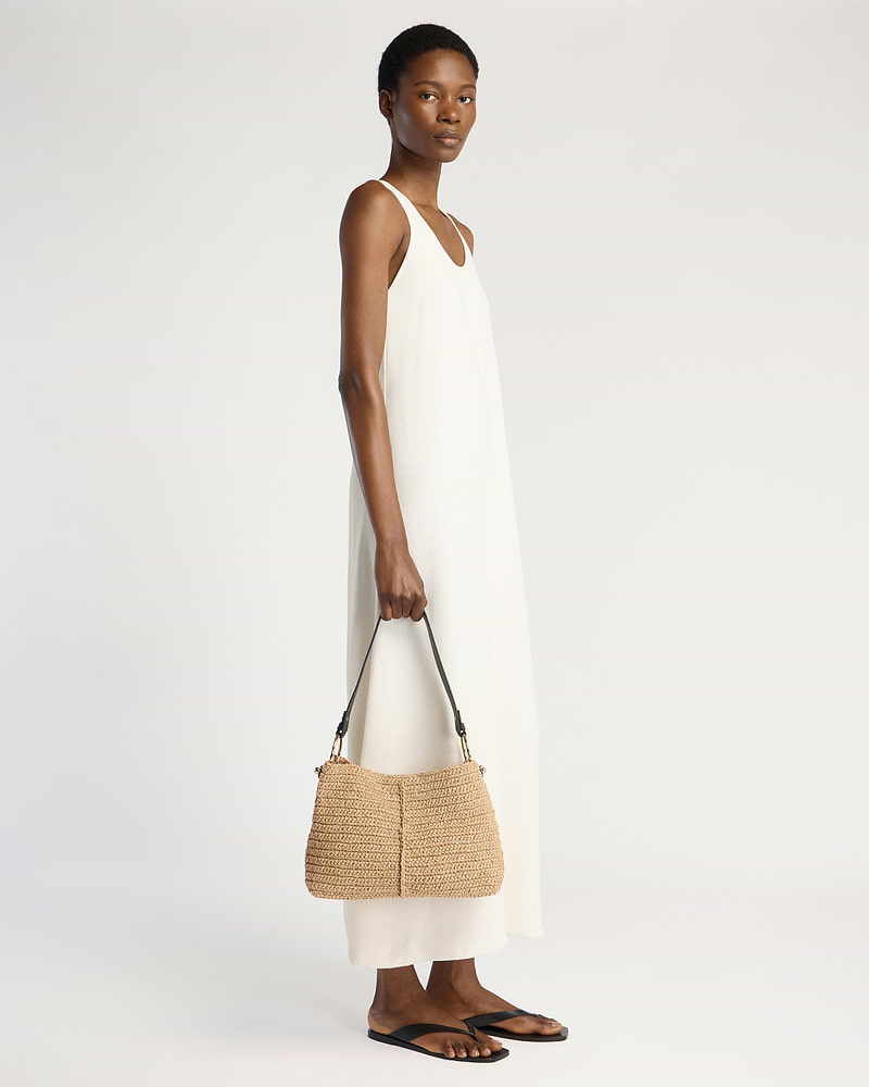 Model in white sleeveless dress holding raffia hobo bag with black strap